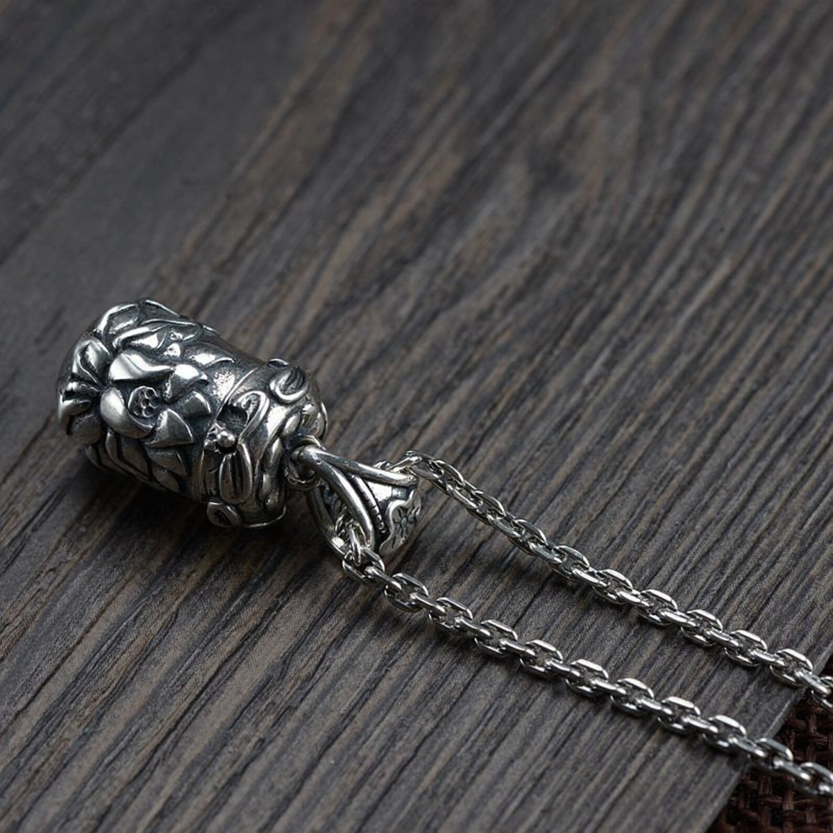 A close-up side view of the closed lotus locket pendant attached to its chain, showcasing the detailed carvings and chain texture against a dark wood background.