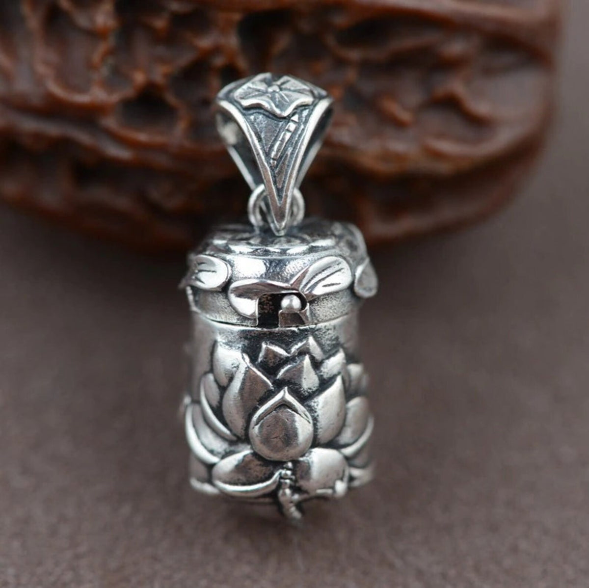 A close-up studio portrait of the closed lotus locket pendant standing upright, highlighting its full design and intricate carvings against a neutral, soft background
