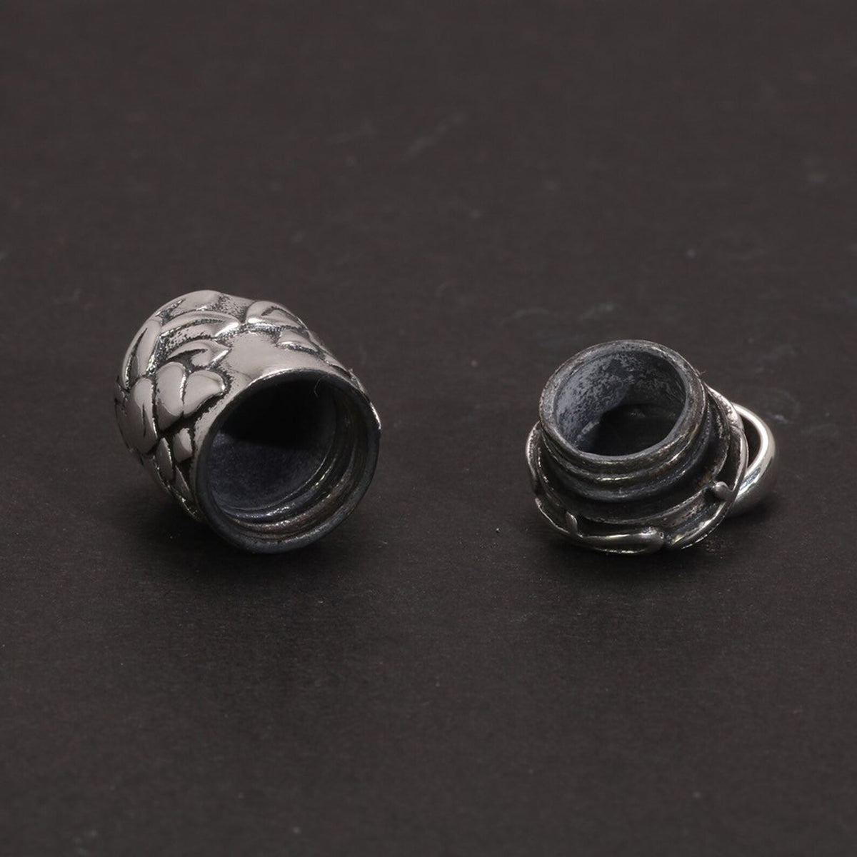 A macro view of the open locket components (the hollow body and the screw-top lid), emphasizing the precise threading and interior detail against a dark background