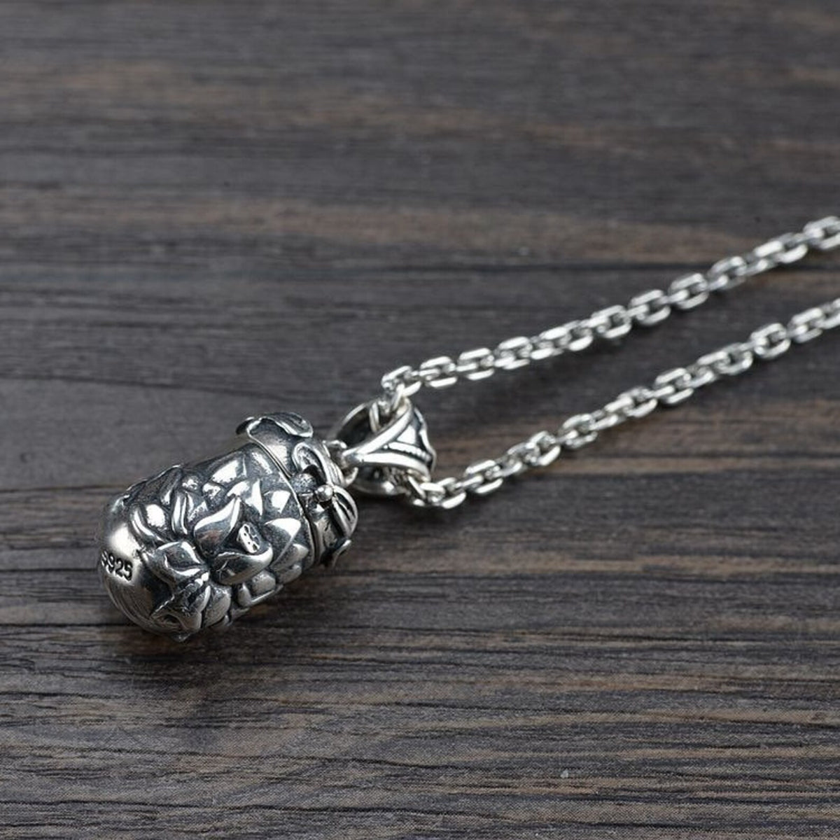 An angled view of the closed silver lotus locket pendant attached to its matching chain, resting on a dark wooden surface