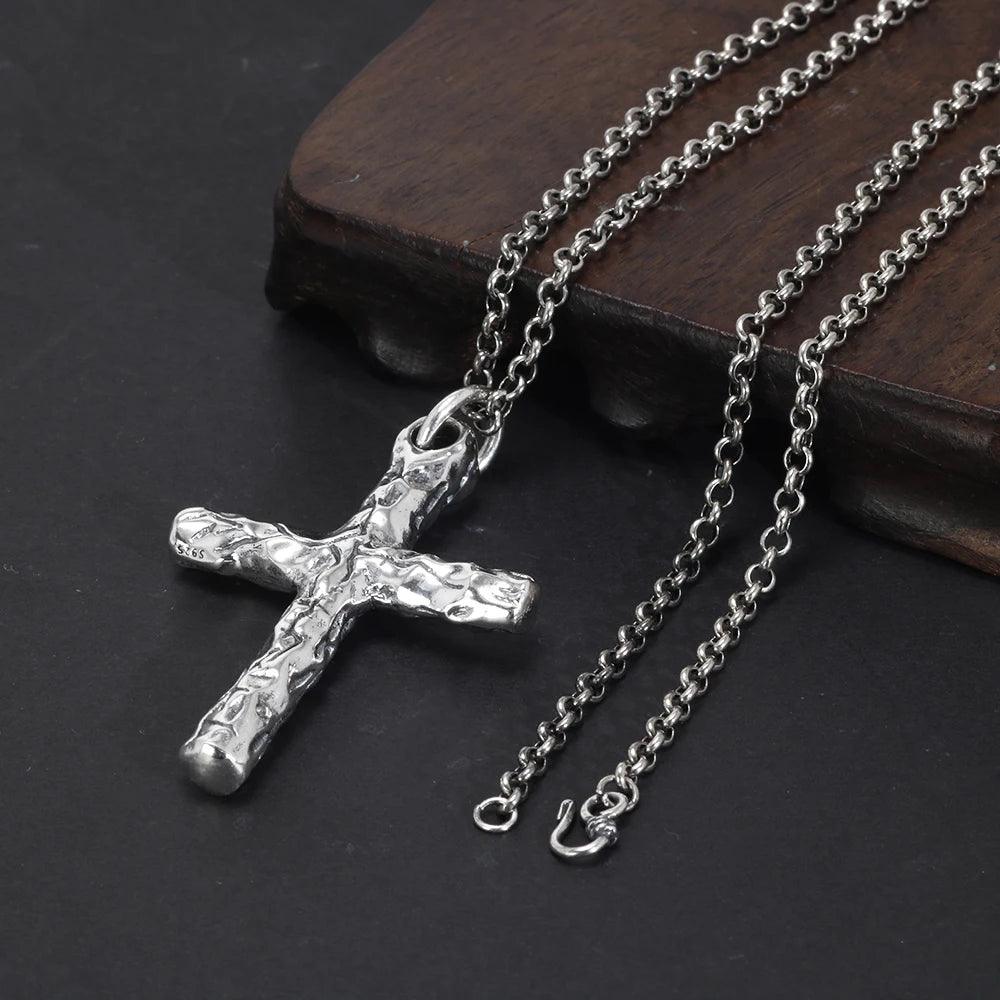Textured silver cross necklace with chain displayed on a dark surface