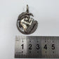 A silver pendant featuring a mermaid curled inside a shell, displayed above a metal ruler to indicate its size on a plain white background.