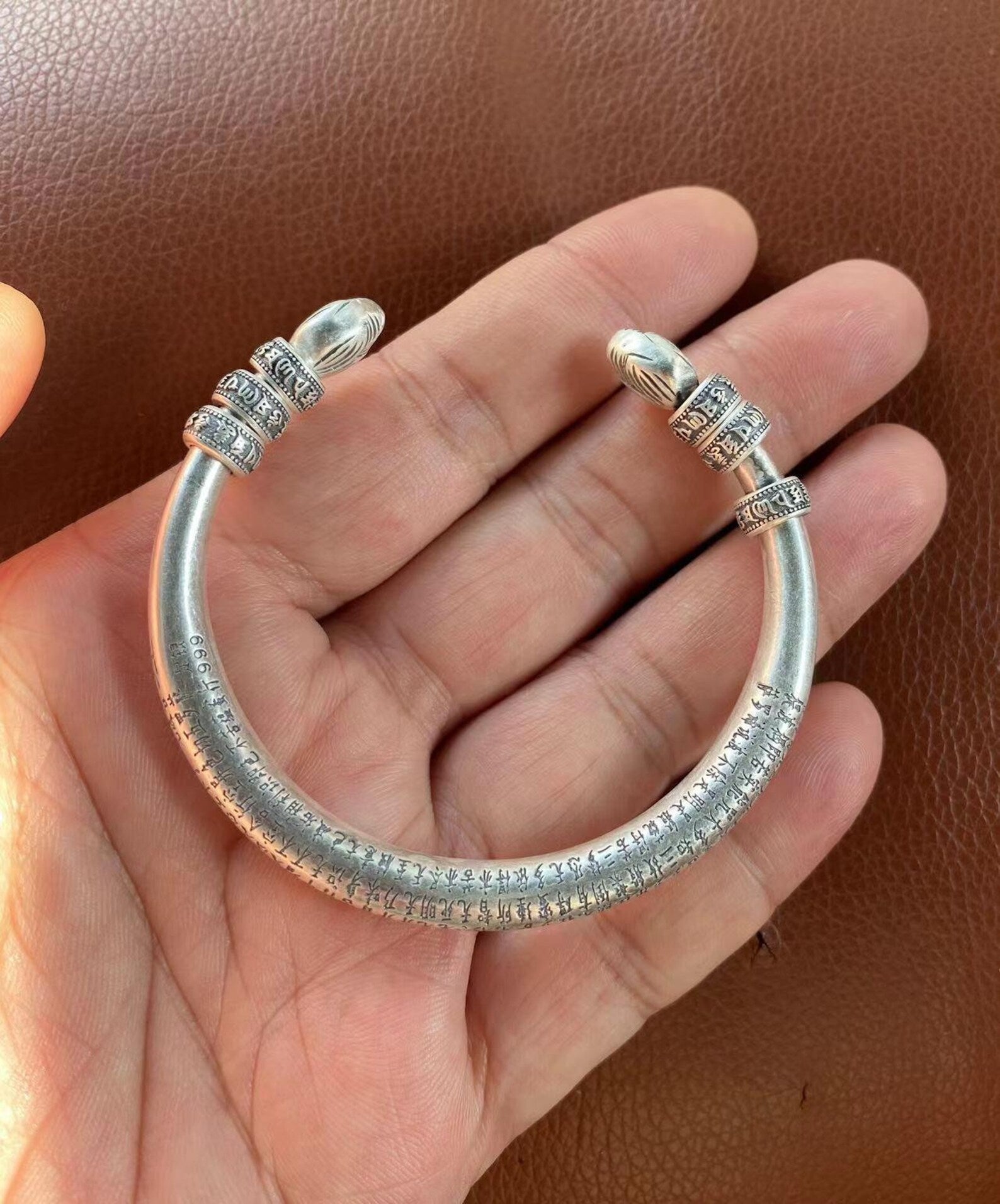 silver tibetan engraved heart sutra bangle bracelet on palm
