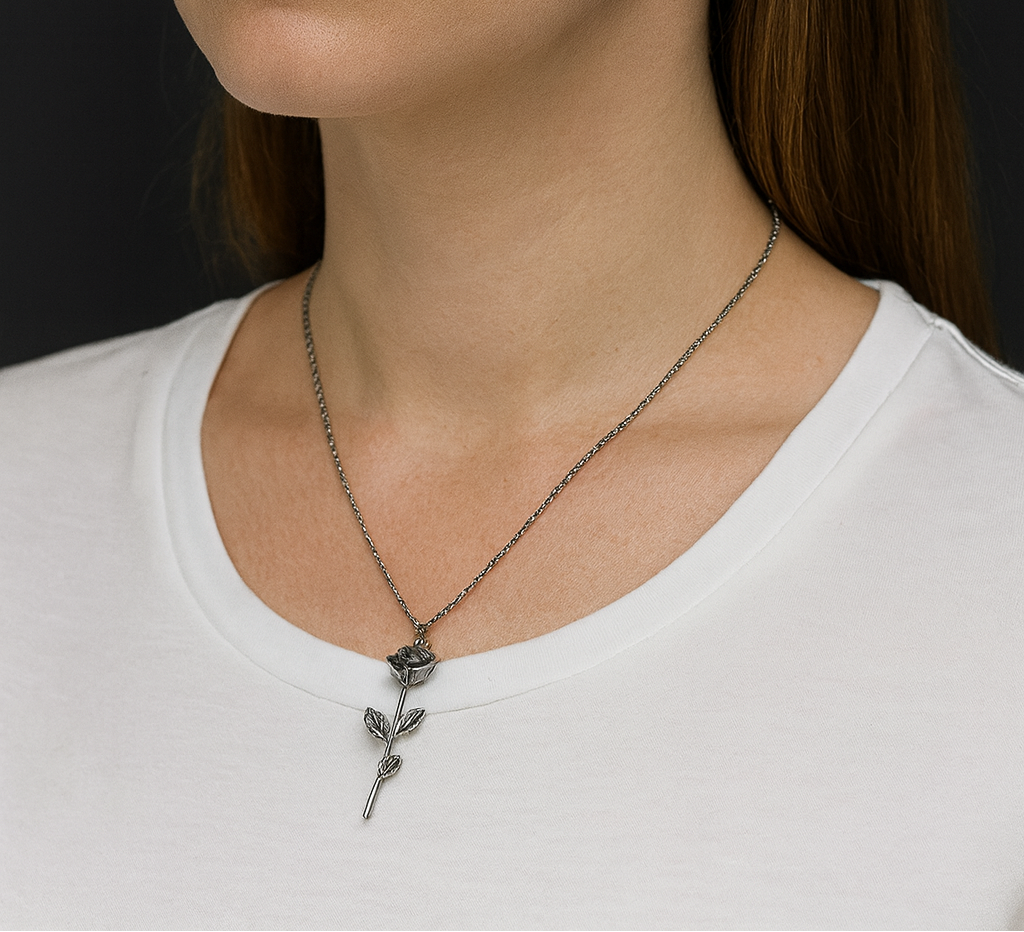 Woman wearing a white shirt with a rose necklace and earrings against a black background